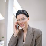 Confident businesswoman with eyeglasses talking on phone in a modern office environment.